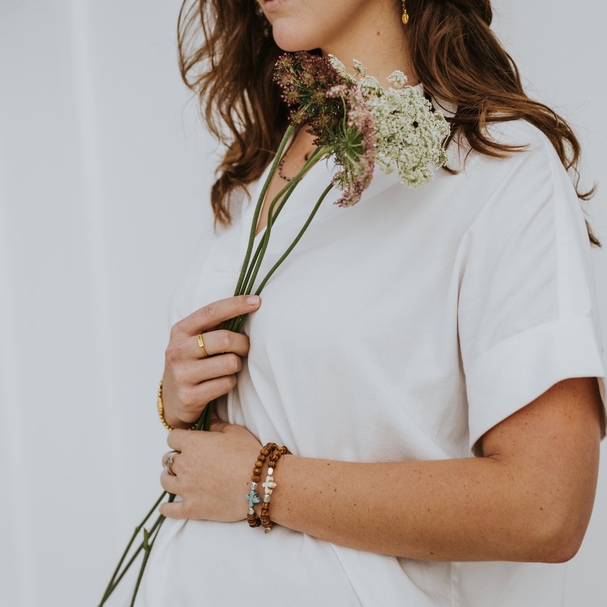 Grounded in Faith Olive Bead Bracelet on a woman with brown hair holding long stem flowers